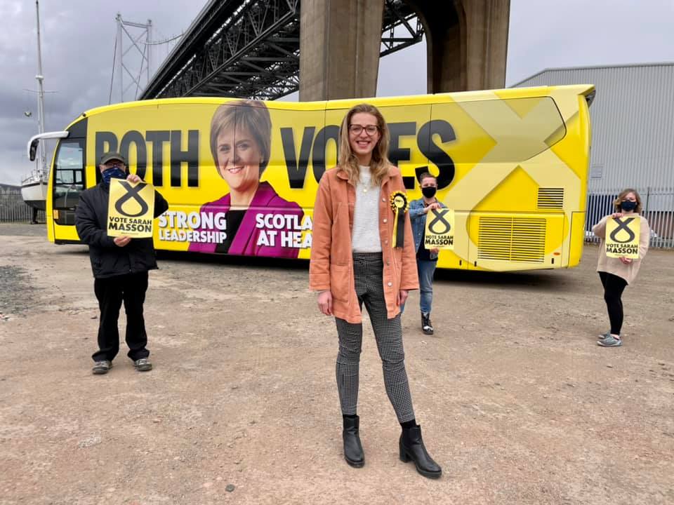 Candidates stand in front of a big yellow both votes snp battle bus under the Queensferry Crossing